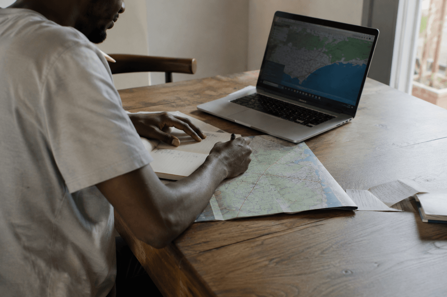 A man working at a laptop with a printed map spread open beside it.