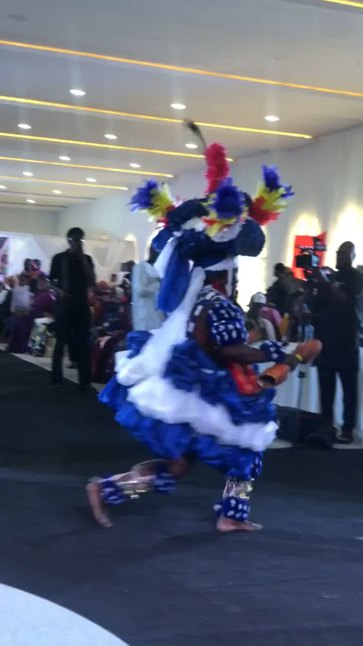 A masquerade dancer performing at an event, filmed from the audience.